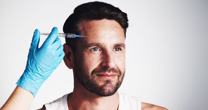 Gloved hand injecting serum into man’s temple against a white background