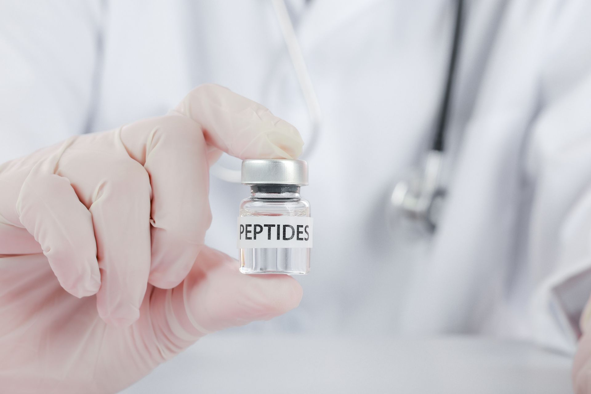Gloved hand holding a small vial labeled “PEPTIDES” against a white clinical background