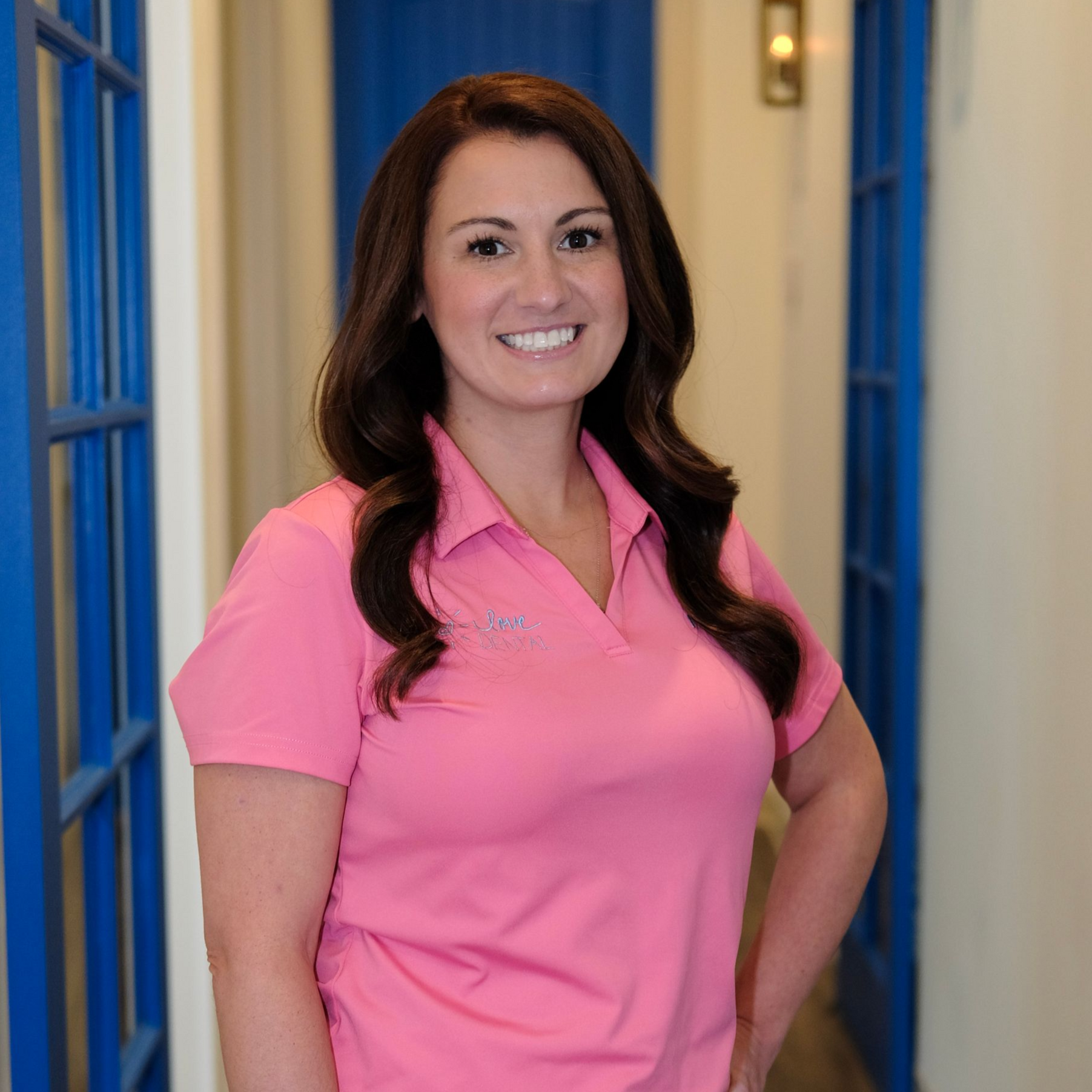 Smiling healthcare worker in blue scrubs and gloves standing in a dental clinic