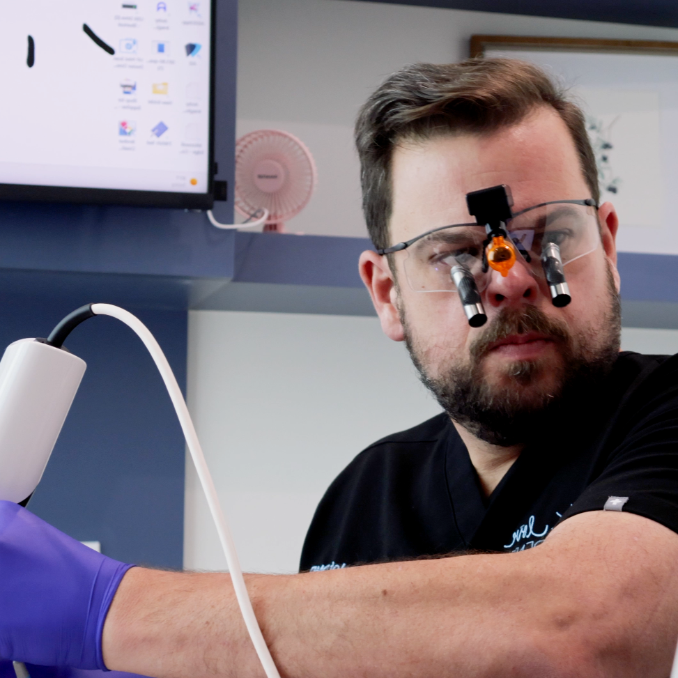 Dental patient smiling in a clinic chair while a dentist works in the background