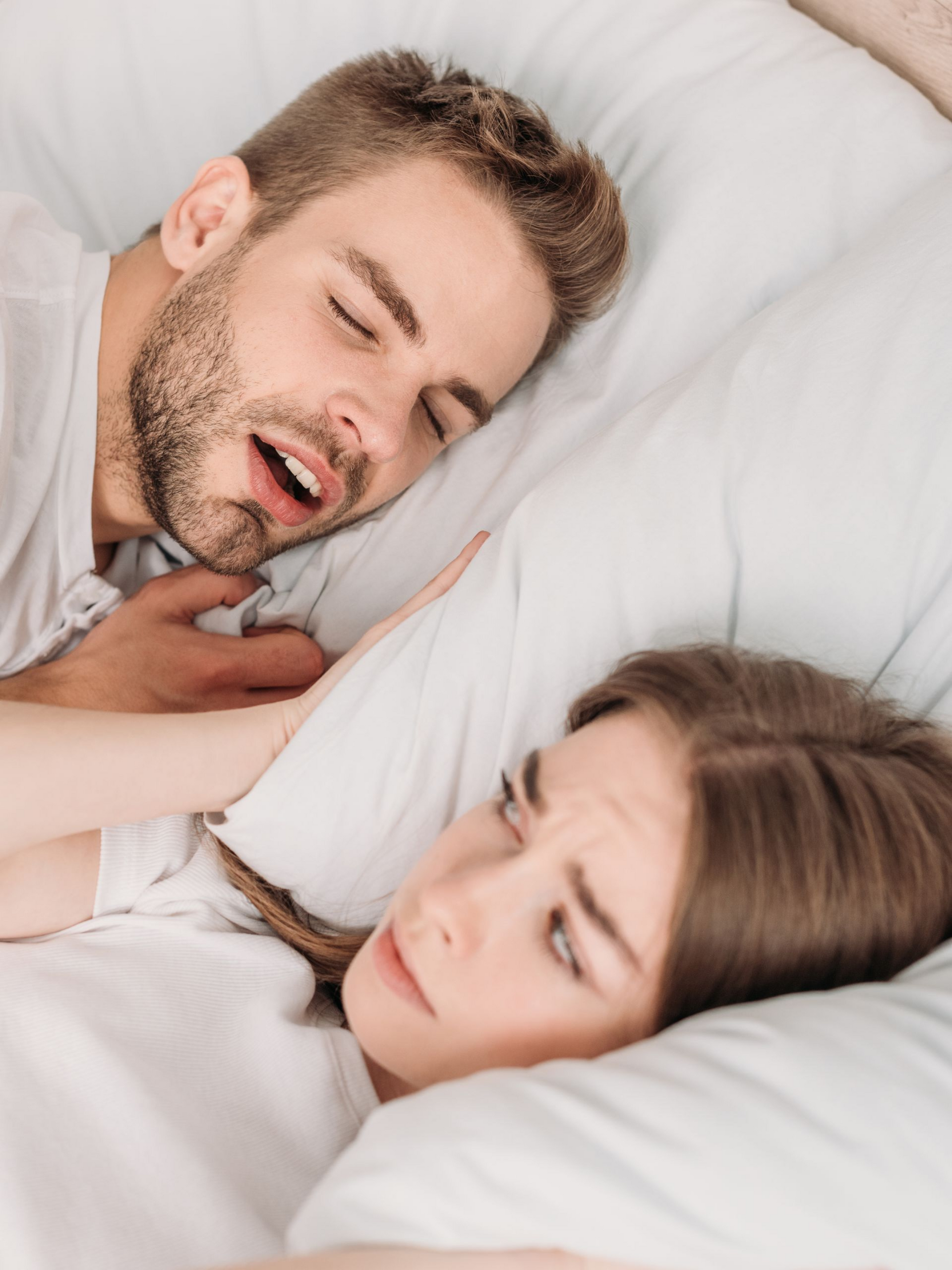 Two people sleeping in bed under white bedding, close together and peaceful.