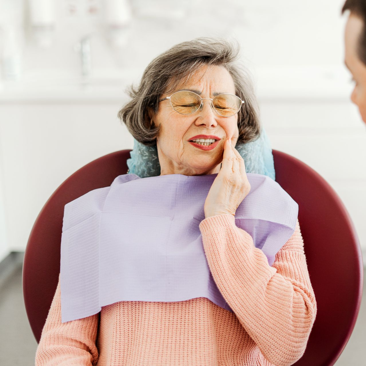 Dentist draping a patient with a lavender bib in a bright clinic