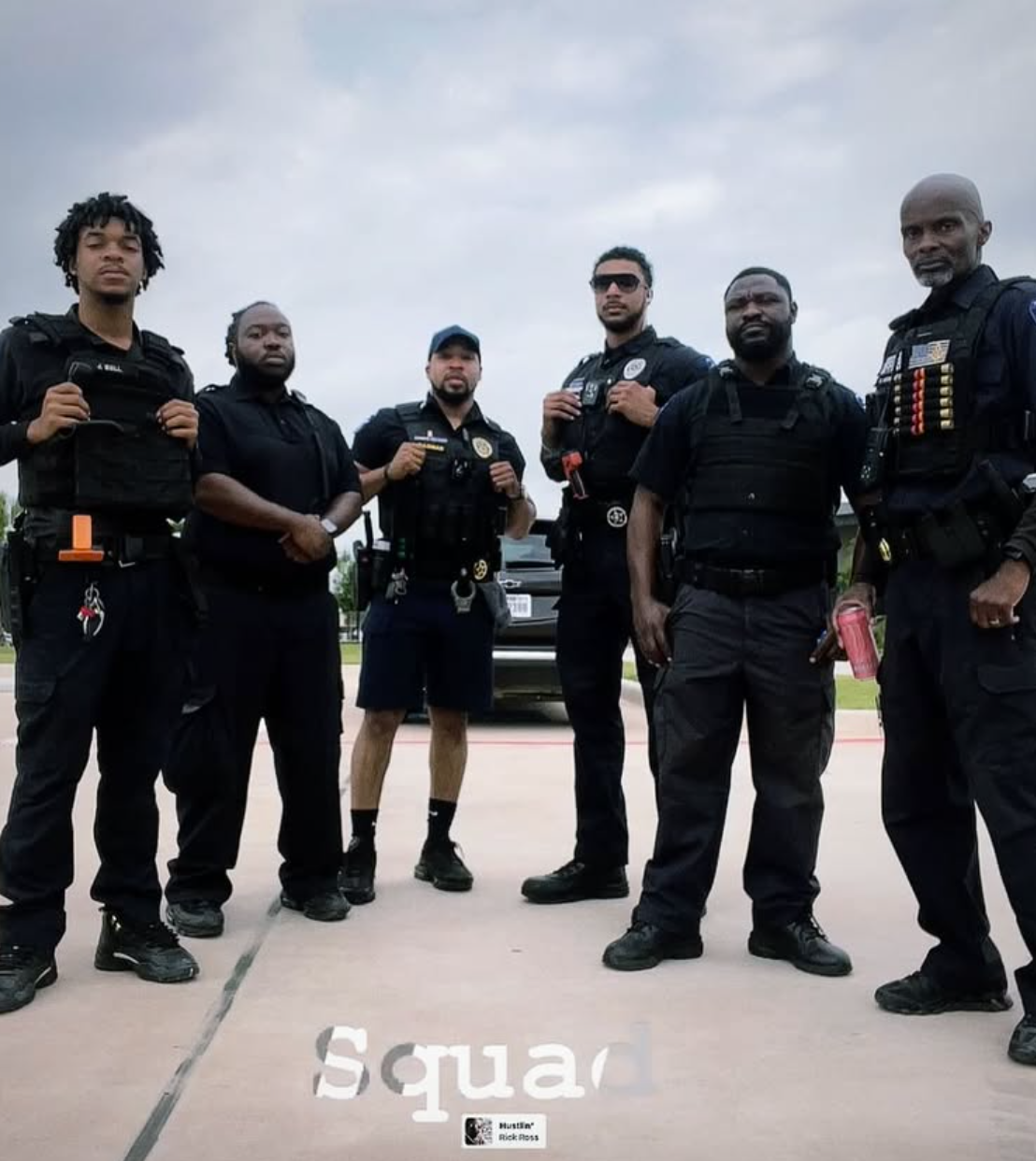 Six Black police officers stand together, in uniform, under a cloudy sky;