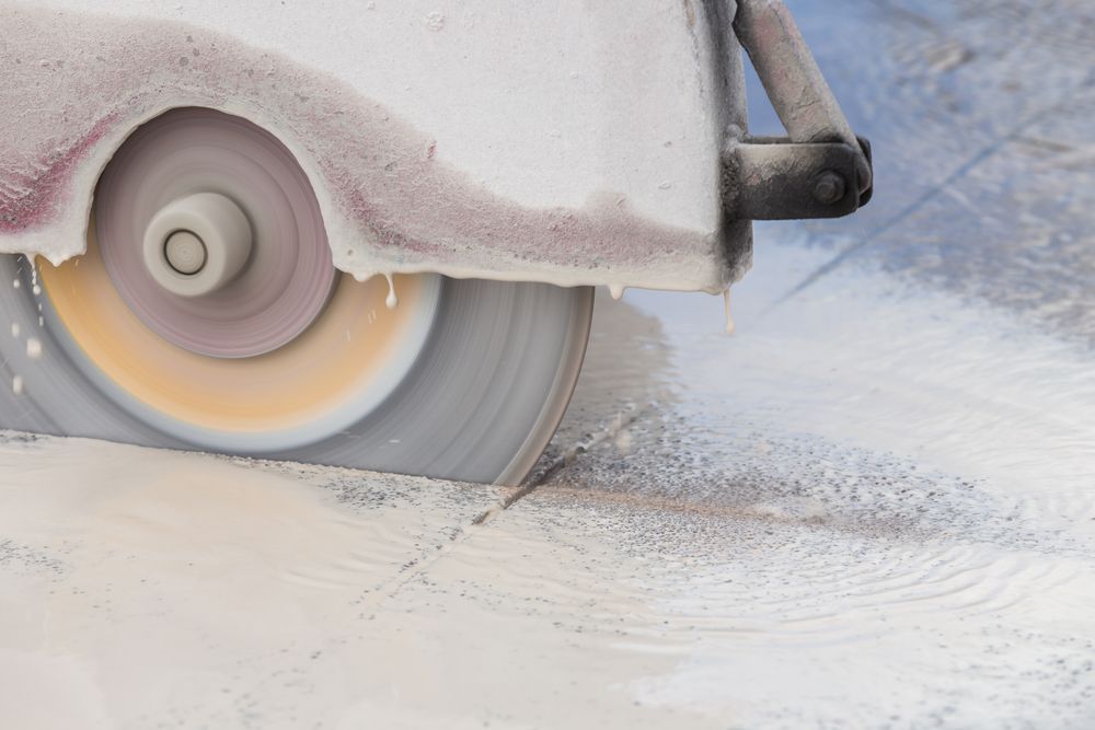 Close-up of a spinning circular saw cutting through concrete, creating dust and debris.