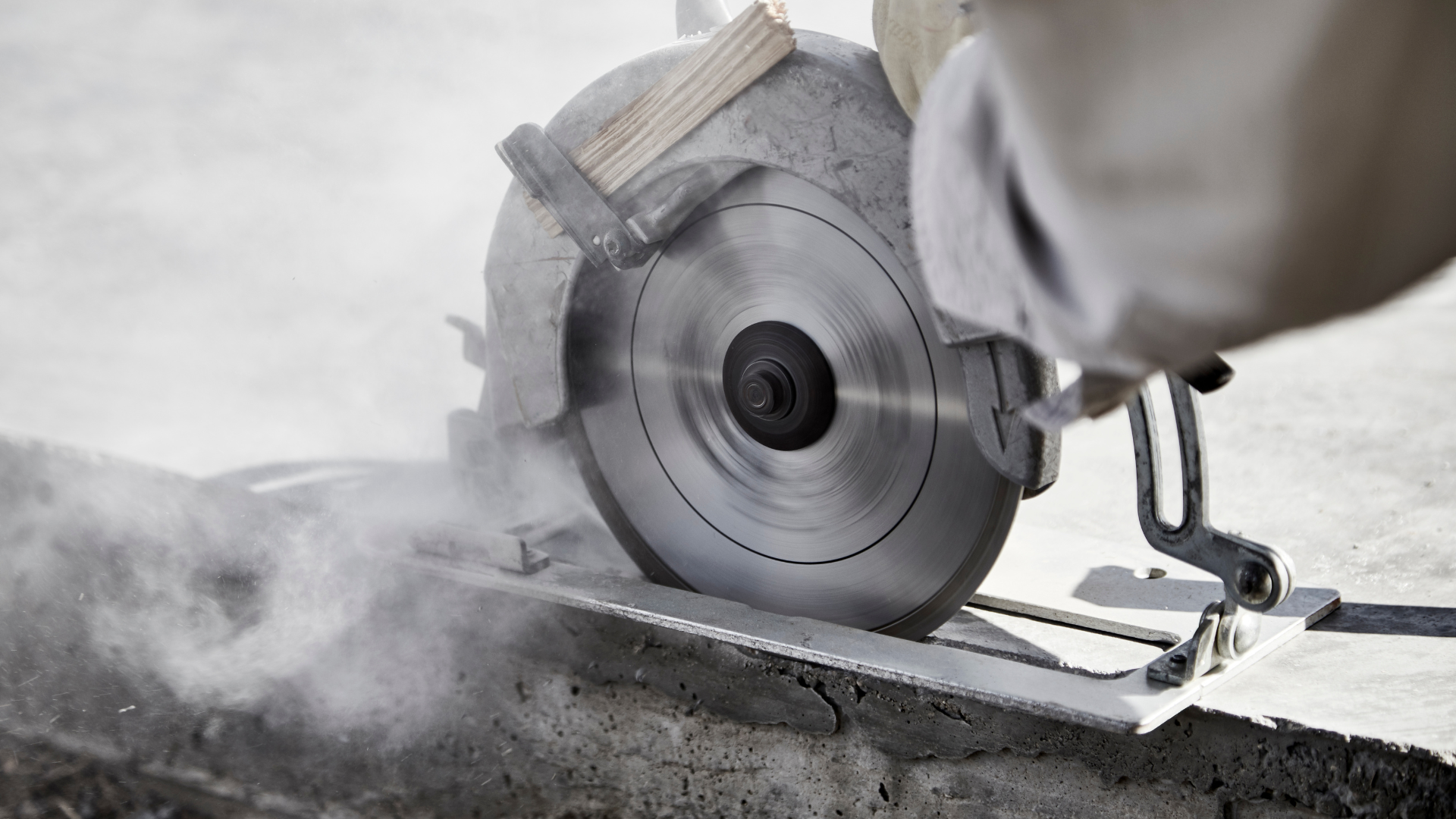 Close-up of a worker using a circular saw to cut concrete, with dust flying.