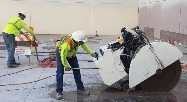 Two construction workers are cutting concrete with a circular saw.