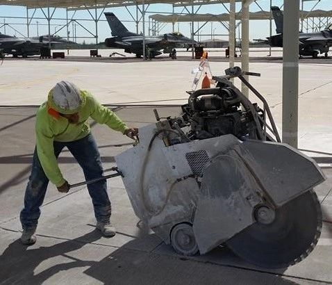 A man is using a machine to cut concrete on a runway.