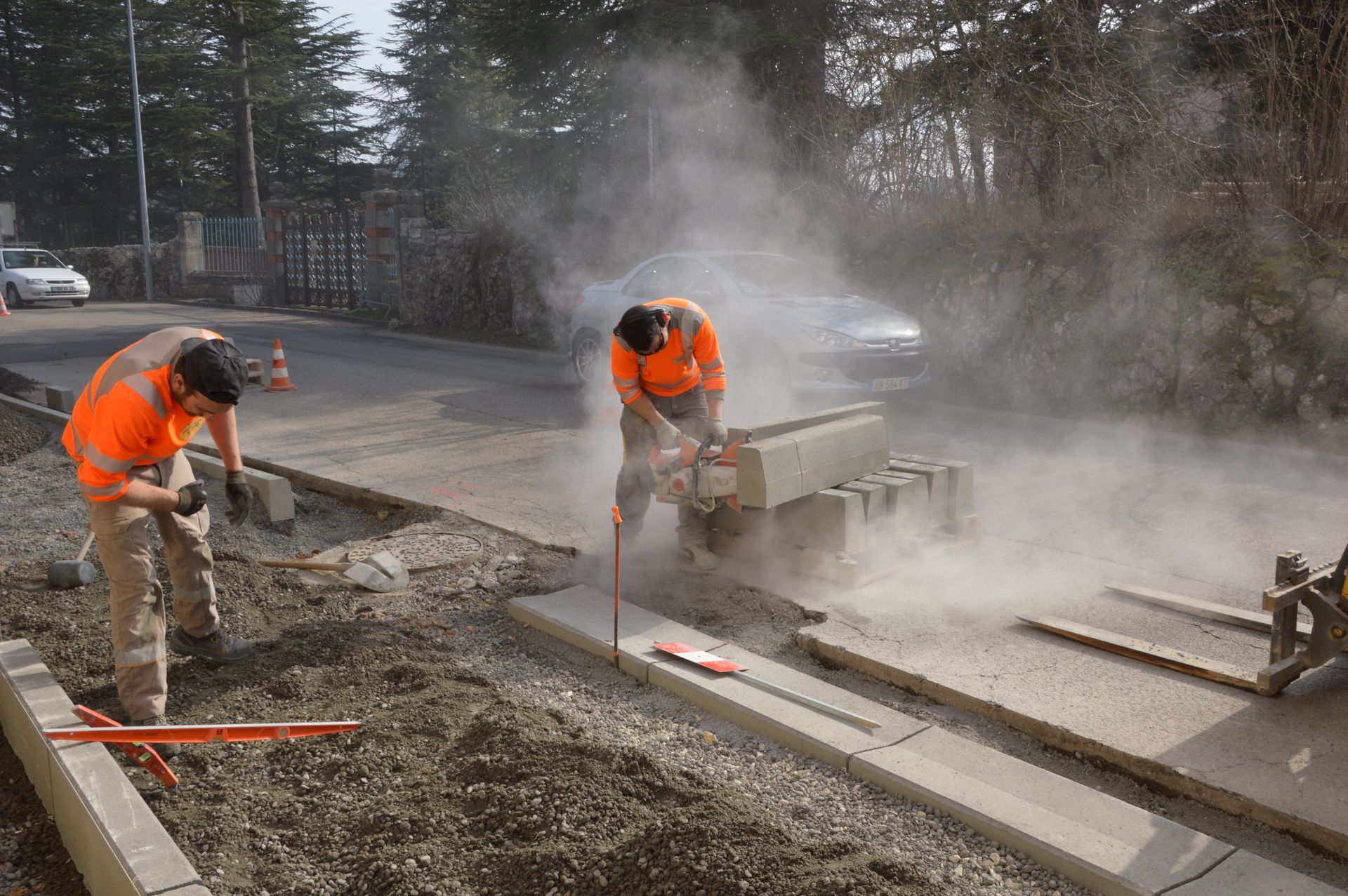 Construction workers in orange safety gear cutting concrete beside a smoky roadwork site