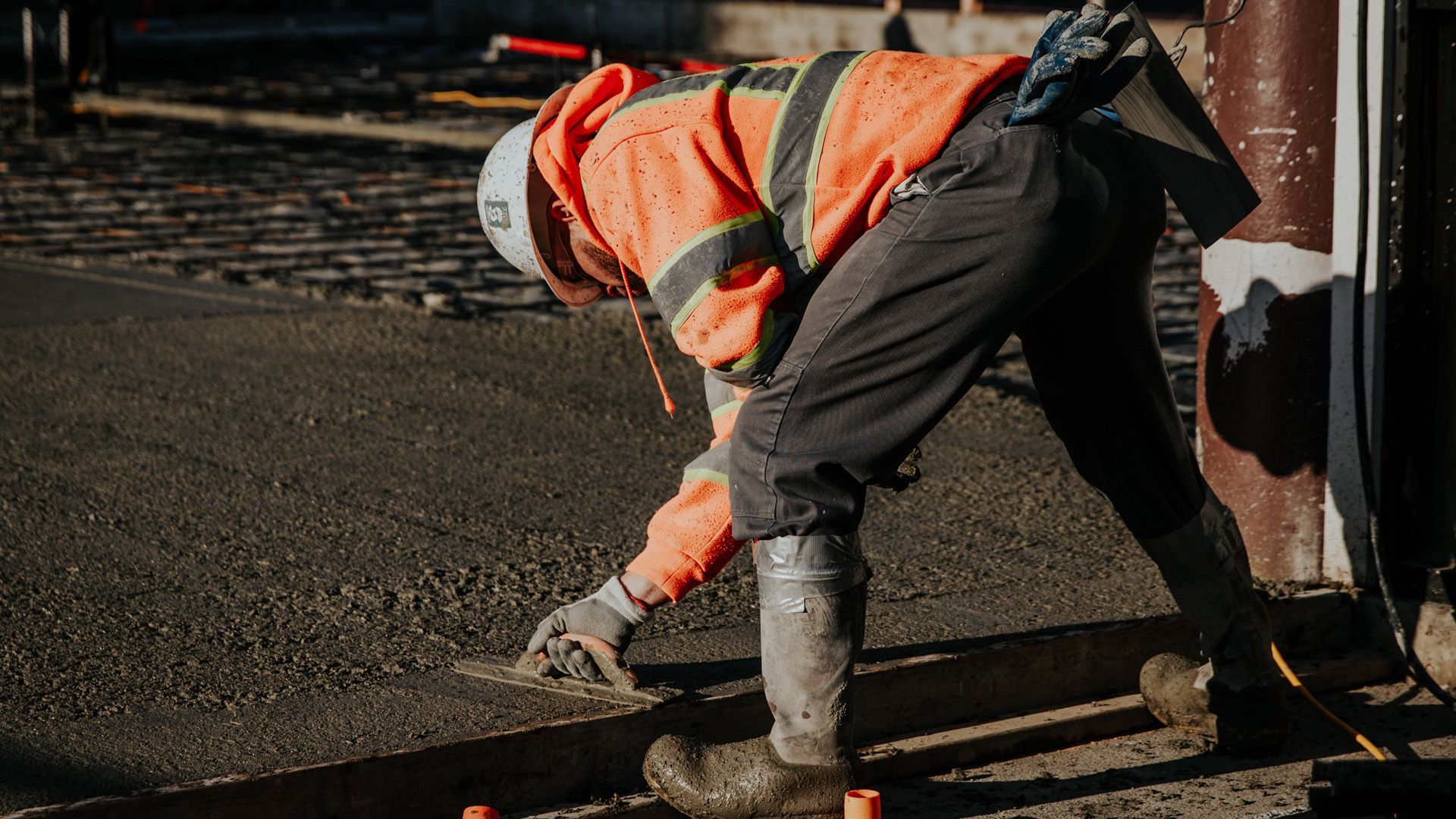 Construction worker in orange vest smoothing concrete with a trowel.