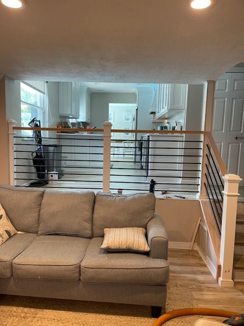 Living room with gray couch, horizontal black railing, view of kitchen.