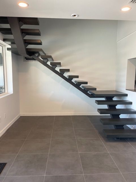 Modern, dark wood floating staircase against a white wall in a room with tiled floors.