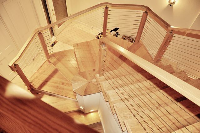 Wooden spiral staircase with cable railings, viewed from above.