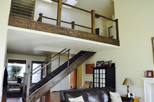 Interior with a dark wooden staircase leading to a loft with railing. Lower level has living room furniture.