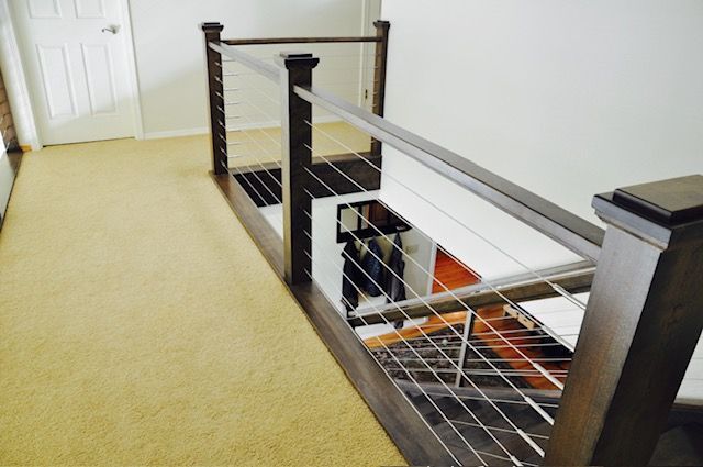 Staircase with wooden posts, stainless steel cables, and brown carpet. Looking down from the top floor.