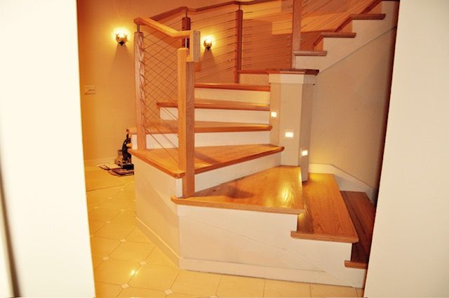 Wooden staircase with white risers, cable railing, and built-in lighting.