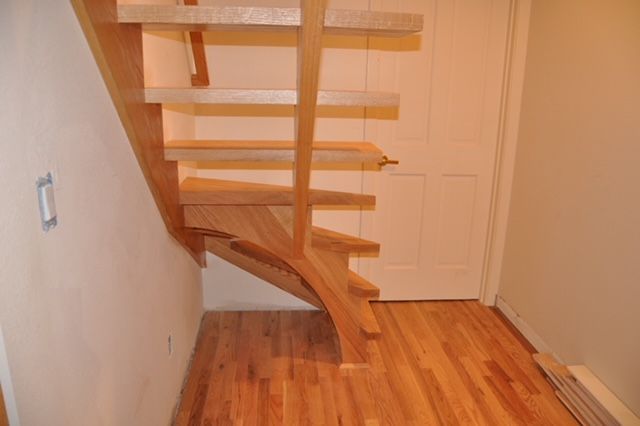 Wooden staircase with open risers, light-colored wood, and curved stringer. Adjacent to a closed door, hardwood floors.