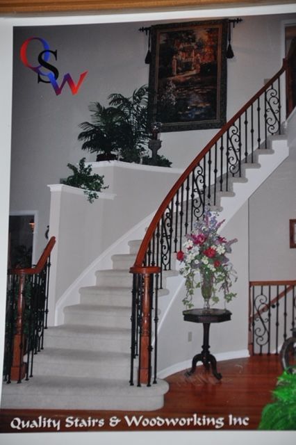 Elegant curved staircase with wood and black metal railings, carpeted steps, and floral decorations.