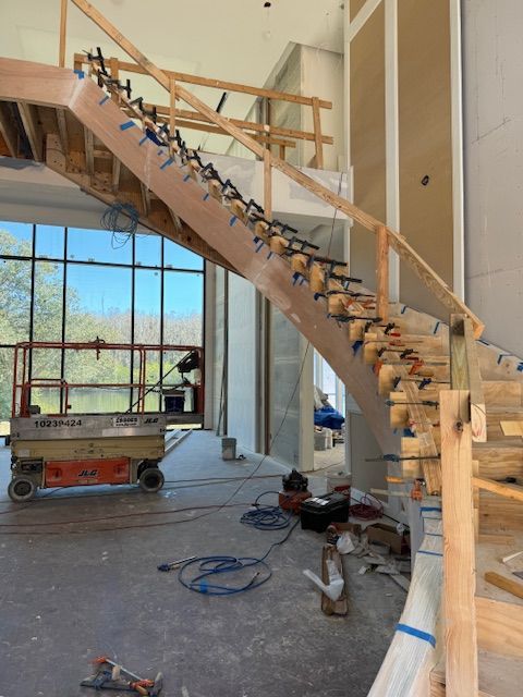 Staircase under construction with clamps, wooden supports, and safety rails. A scissor lift is visible in the background.