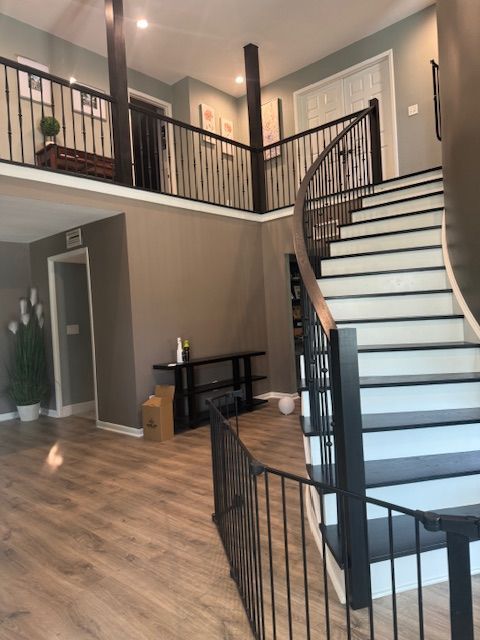 Spacious foyer with a winding staircase, dark railing, and wooden flooring. 