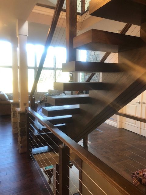 Wooden staircase with floating steps and cable railing. Natural light from a window.