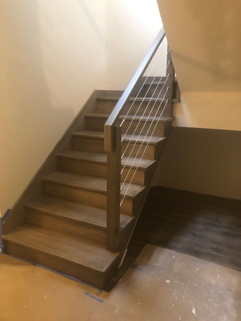Wooden staircase with metal cable railing, tan walls, and a light brown floor.