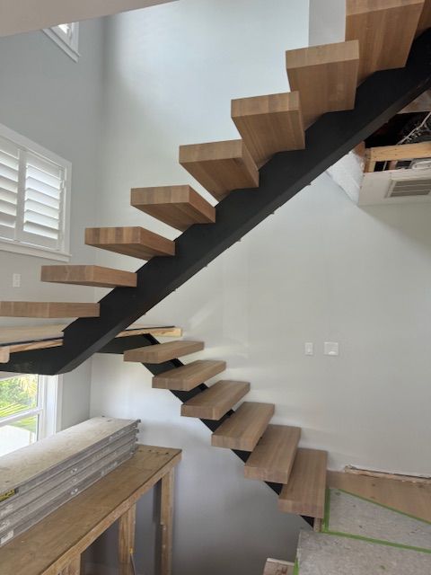 Floating wooden staircase with black support against a light gray wall.