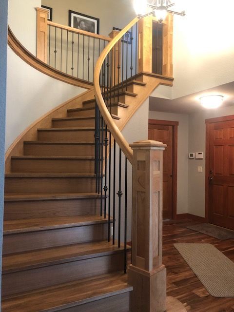 Wooden curved staircase with black metal balusters and wood railing. Entryway setting.
