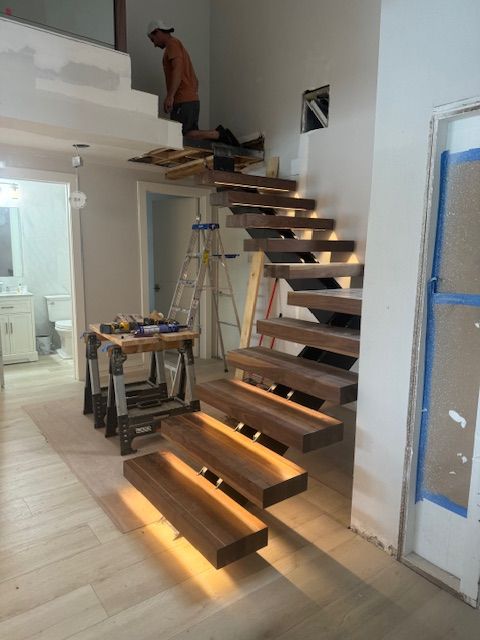 Floating wooden staircase under construction; worker on landing, tools nearby.