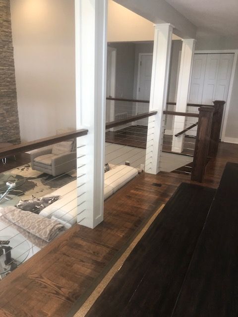 Interior view: dark wood railing and floor with white pillars, metal cable and wood railings above.