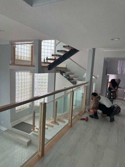 Workers install glass and wood railing on a modern staircase, with visible construction tools.