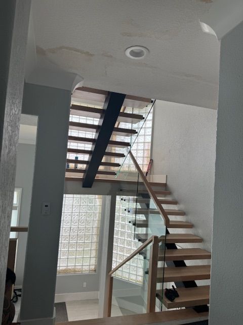 Modern interior staircase with glass railings and wood steps. Glass block wall and black support beam.