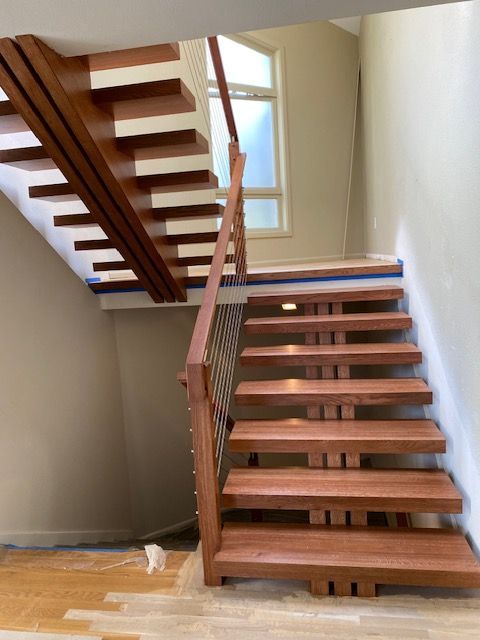 Wooden floating staircase with a metal handrail, leading up to a window.