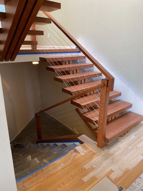 Wooden staircase with cable railing, indoors. Brown steps and supports, white walls.