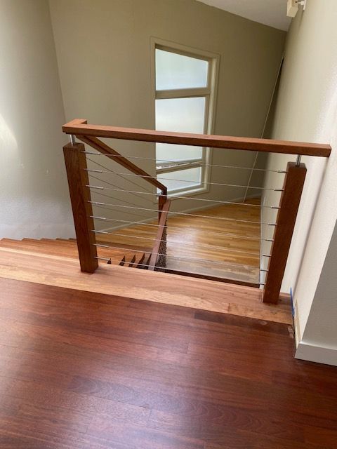 Wooden staircase with stainless steel cable railing. Interior shot, natural light, hardwood floors.