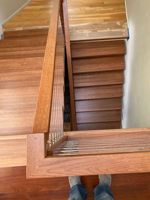 Wooden staircase with banister, viewed from above. Person's feet visible.