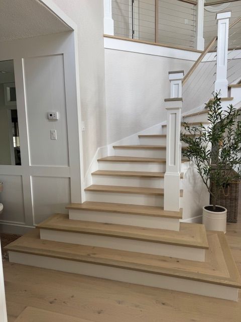 Light-wood staircase with white risers and trim, ascending to a second story, in a neutral-toned home.
