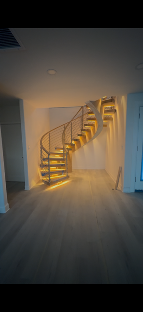 Spiral staircase with wood steps, illuminated by warm lights, in a modern, light-filled space.