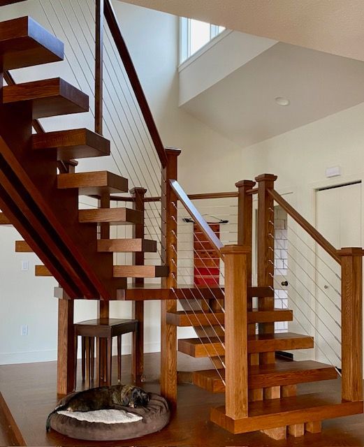 Wooden staircase with a cat in a bed at the base, and cable railing.
