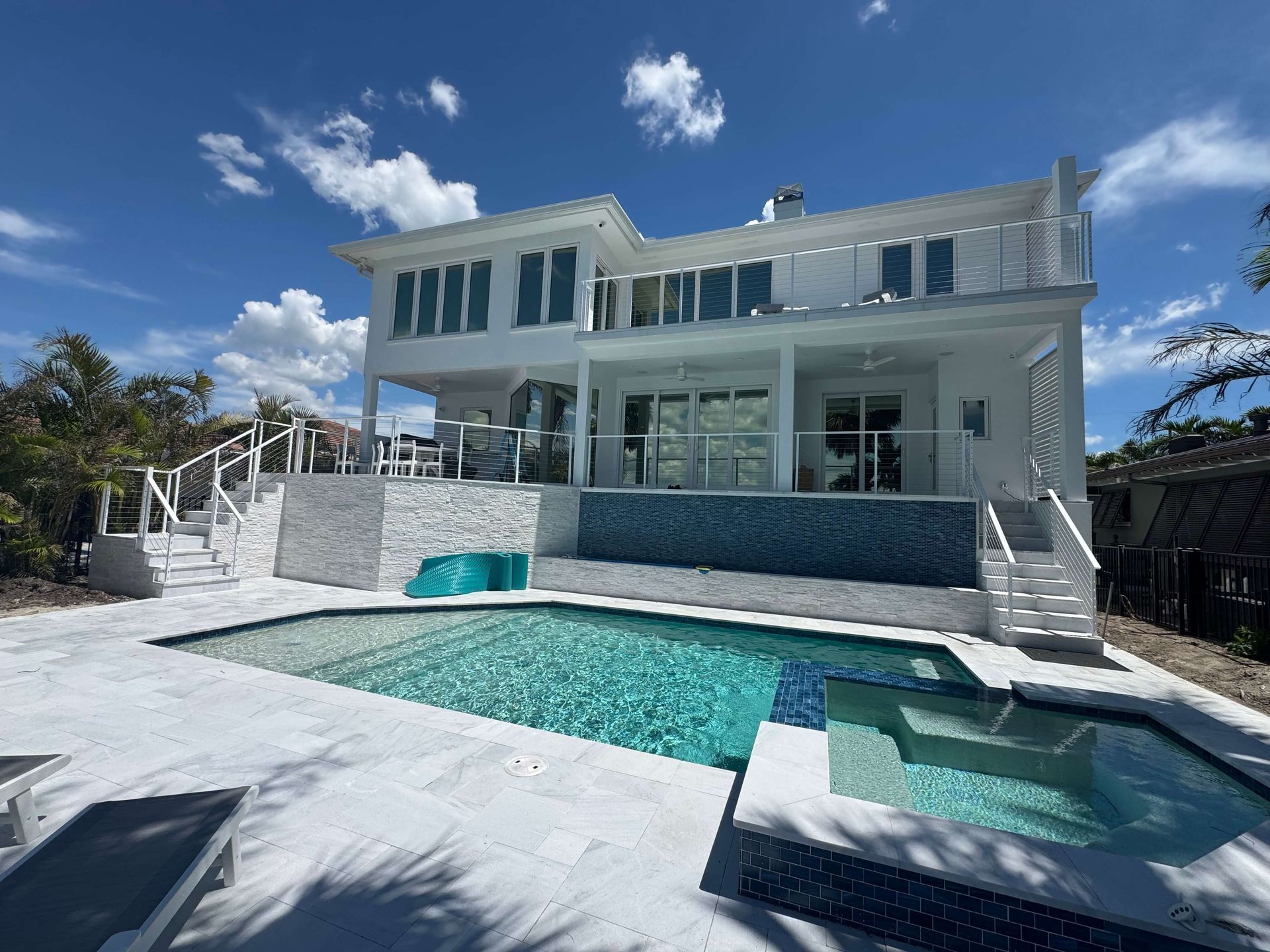 White multi-story house with a pool and hot tub, blue sky.