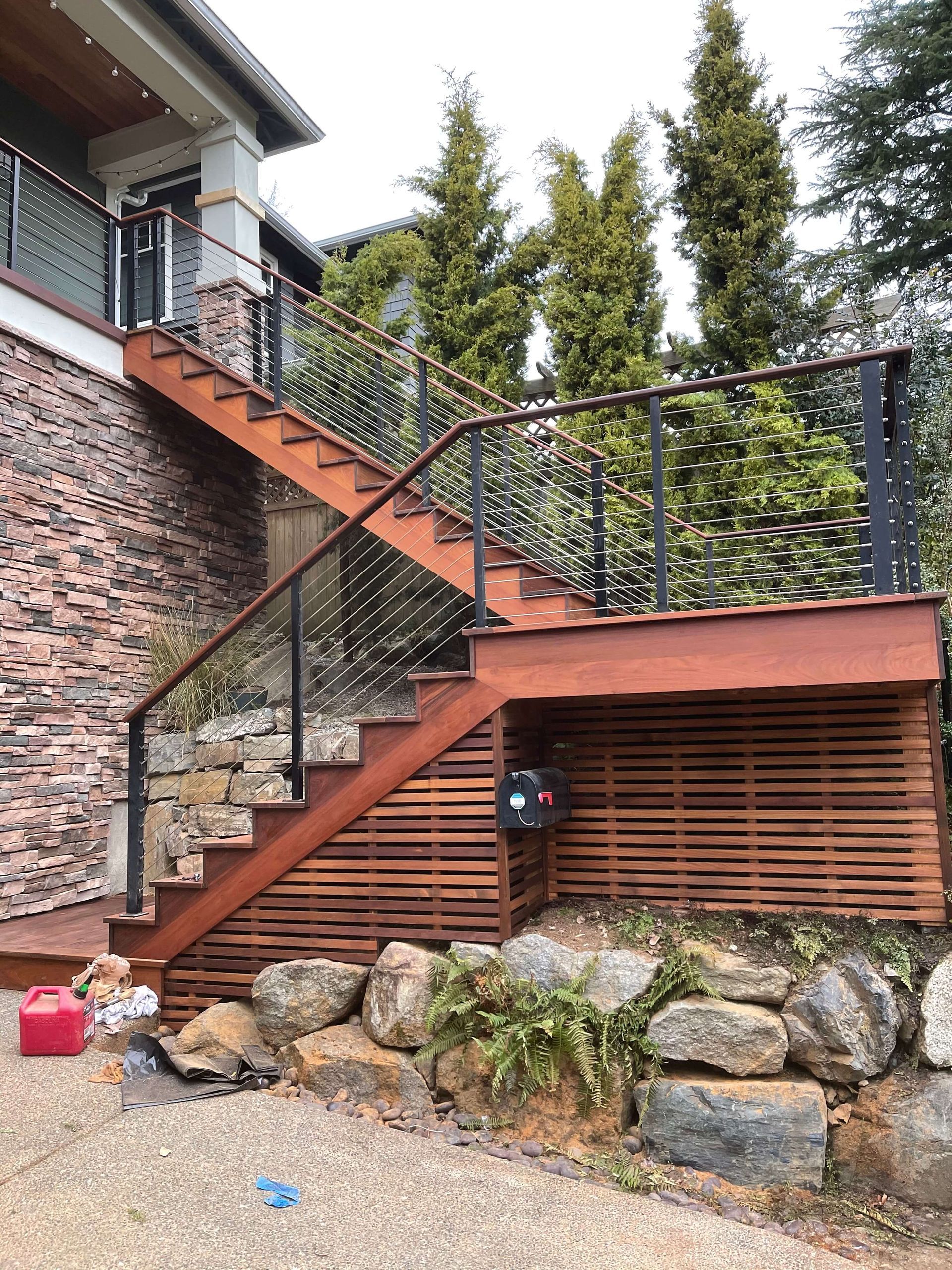 Wooden stairs with black railings lead up to a deck, set against a stone and wood exterior.