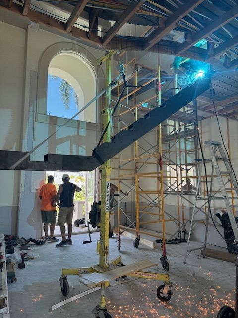 Construction: workers welding metal beams inside a building with scaffolding and a lift. Sparks fly.