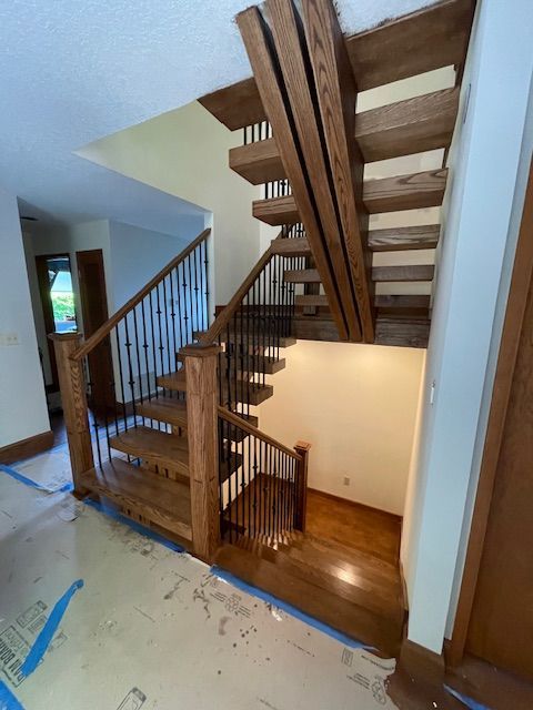 Wooden staircase with black metal balusters in a brightly lit hallway.