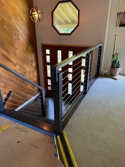 Stairway with metal and cable railing leading to a doorway, wood paneling on the left, carpeted floor.
