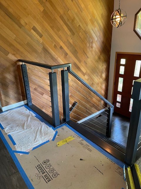 Modern stair railing with cable infill and wood paneling on the wall.