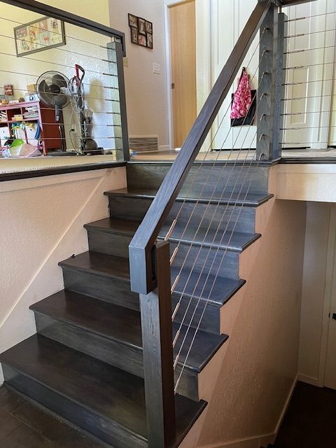 Staircase with wooden steps and a cable railing system. Dark wood, neutral walls, and a view into a home.