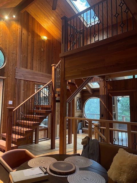 Wooden interior with staircase leading to a mezzanine, two round windows, and a skylight.