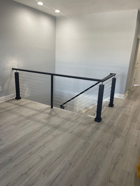 Modern black metal railing with cable infill along a staircase landing, gray walls, and light wood-look flooring.