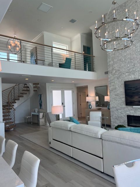 Spacious living room with a loft, white furniture, and a stone fireplace. A spiral staircase leads upstairs.