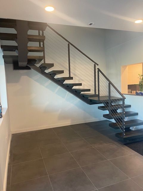 Modern floating staircase with gray treads and cable railing against a white and light blue wall.