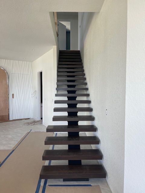 Modern wooden staircase with black central support, ascending to a hallway.